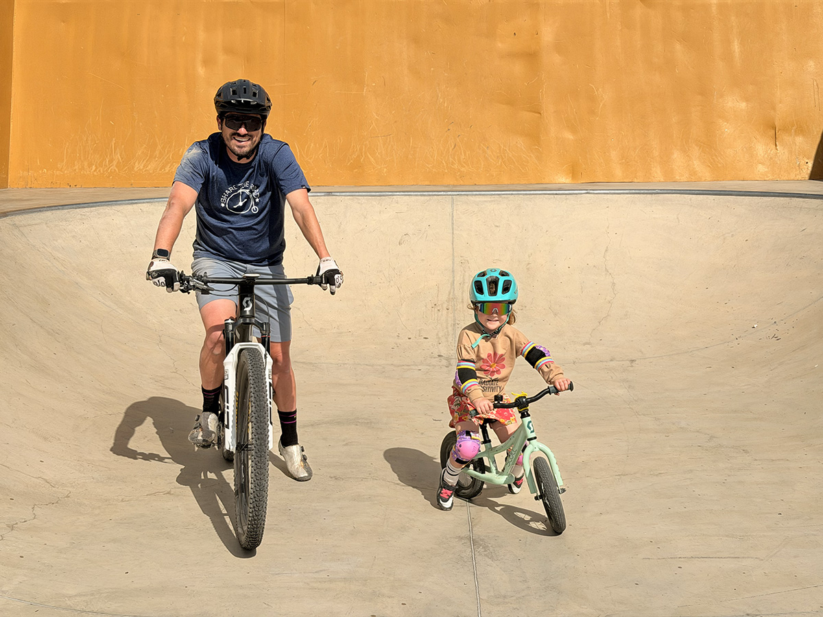 Steven riding in a skate park bowl alongside his young daughter Emi on a balance bike