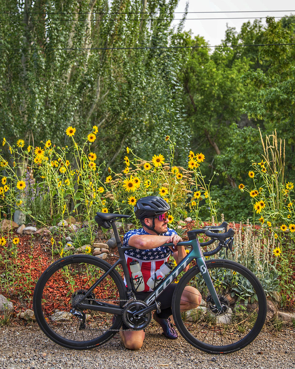 Steven in a Stars and Stripes cycling jersey beside his road bike, sunflowers in the background