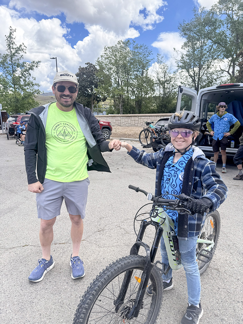 Steven fist-bumping a young athlete named Oliver beside his mountain bike at the CAF APEX MTB Weekend